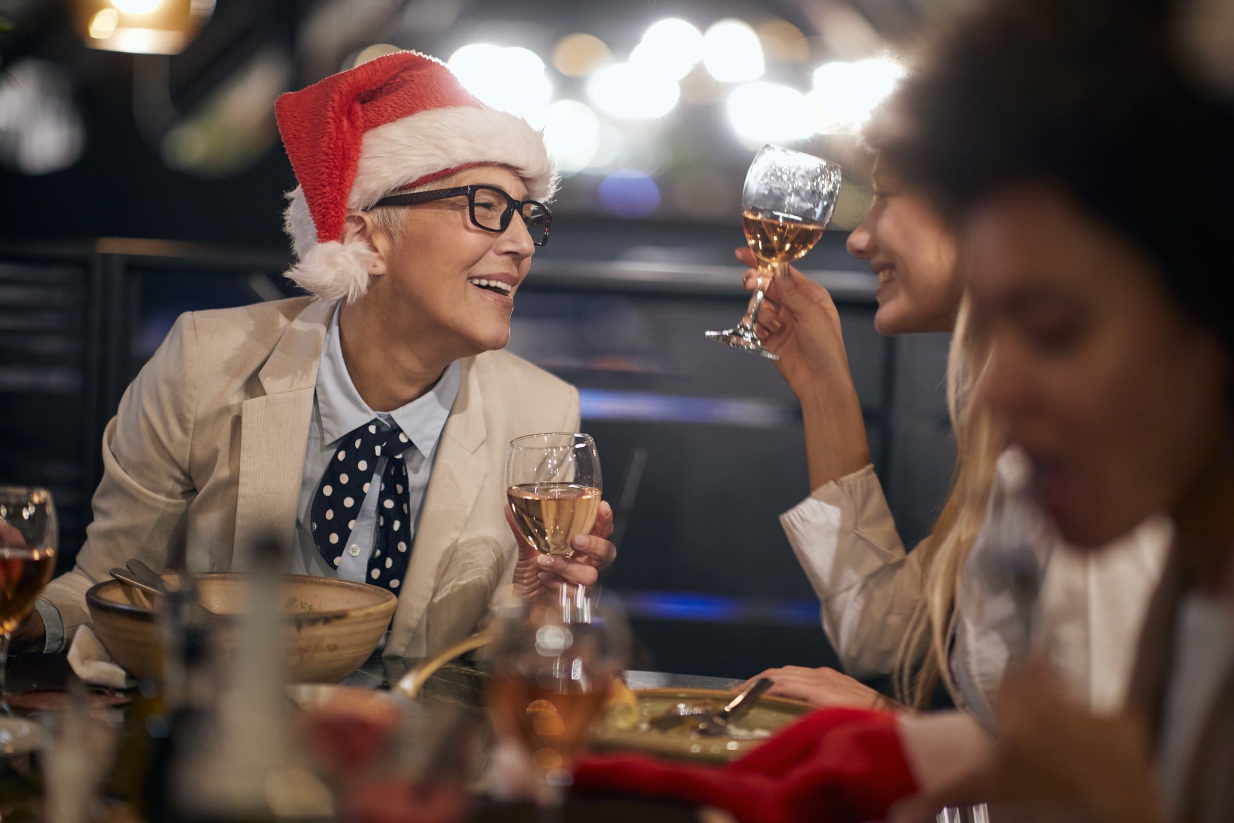 159815043_m caucasian boss lady wearing santa hat with glasses having a good time at business dinner at the end of successful year with colleagues